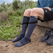 Person wearing a pair of of Injinji Trail Midweight Over the Calf – Performance Toe Socks in Granite -  gray toe-separated socks outdoors on a natural background . Buy now at ICEGRIPPER.