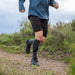 Person running on a trail wearing blue shirt, black shorts, and Injinji Trail Midweight Over the Calf Performance Toe Socks in Granite. Gray with black accents. Anatomical fit toe socks promotes natural toe splay resulting in total foot utilization, which supports full-foot alignment and engagement. Buy now at ICEGRIPPER.