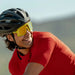Person wearing a red cycling outfit with a helmet and yellow sunglasses, outdoors. The High Voltage Campeone is built around Knockaround’s innovative Knockterra performance lens technology, Campeone sunglasses deliver crystal-clear vision, UV400 protection, and impact-resistant durability. Their sleek wraparound design guards against low winter sun and glare reflected from snow and ice, while rubberized adjustable nose grips and flexible non-slip arms ensure a secure, all-day fit.