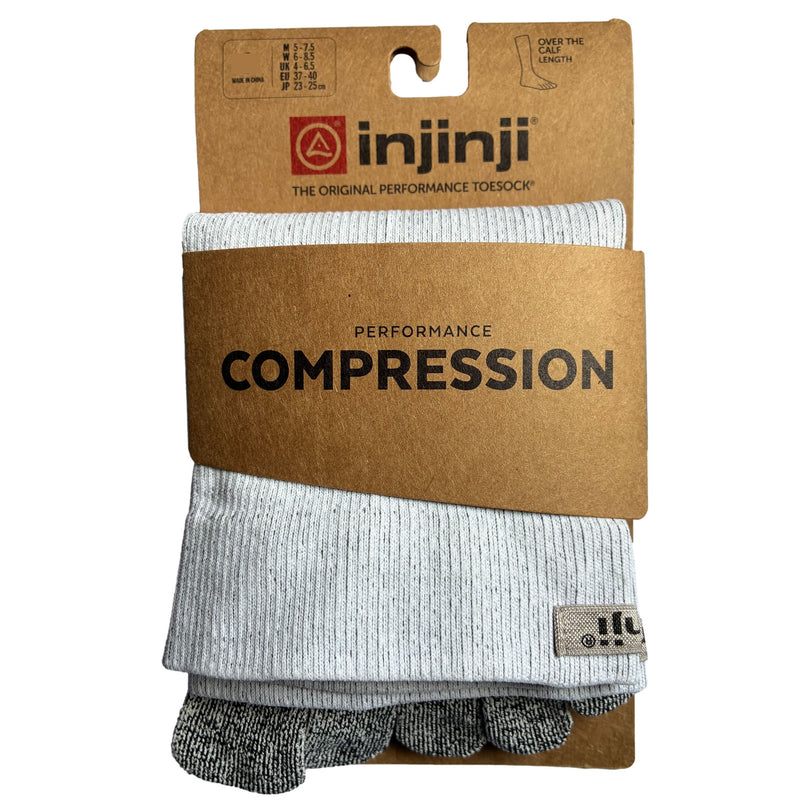 Pack shot. Injinji Compression Over the Calf Toe Socks. Buy now at ICEGRIPPER. A pair of light gray ribbed compression toe socks folded inside a brown kraft paper blister card by injinji, with the brand name and 'PERFORMANCE COMPRESSION' printed on the packaging.