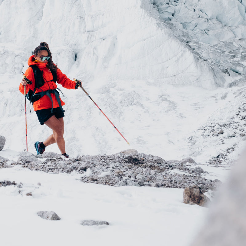 Person in orange jacket hiking on a snowy mountain using the new Kahtoola Microspikes Ghost Footwear Traction. Us the Ghost wherever you might need to pack light and move fast.