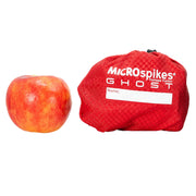 Orange Red Microspikes Ghost shoe cover drawstring bag next to an apple on a white background. Demonstrating the compact size that the new Kahtoola Microspikes Ghost Footwear Traction can be folded down to/