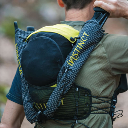 A close-up back view of a person wearing an INSTINCT Trail Vest  with the Instinct Ergo Quiver 2 from ICEGRIPPER, attached. He is taking out one of his Running Poles.