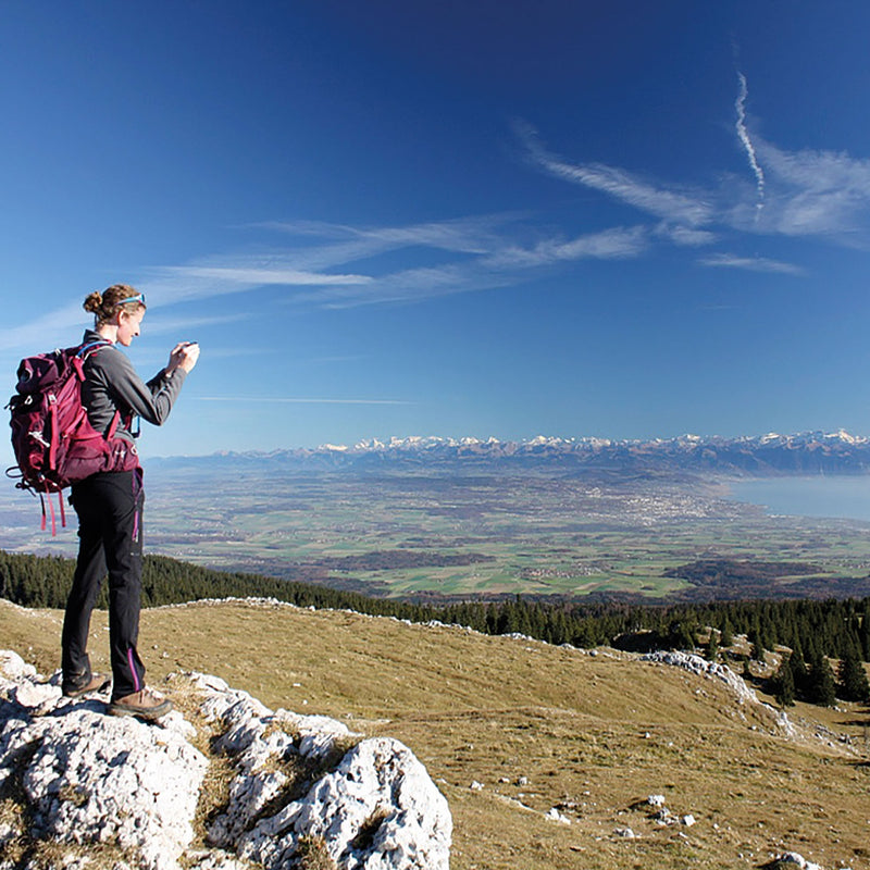 Hiker with a backpack looking towards the peaks of the High Alps, while walking the Jura Crest.