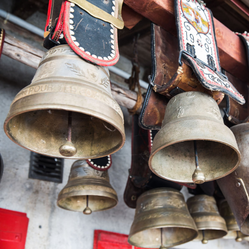 Vintage brass bells hanging with a leather saddle in the background. You might see these while walking Switzerland's Jura Crest Trail. The 14 stages of a proposed exploration are detailed in the Switzerland's Jura Crest Trail Guide Book now available at ICEGRIPPER.