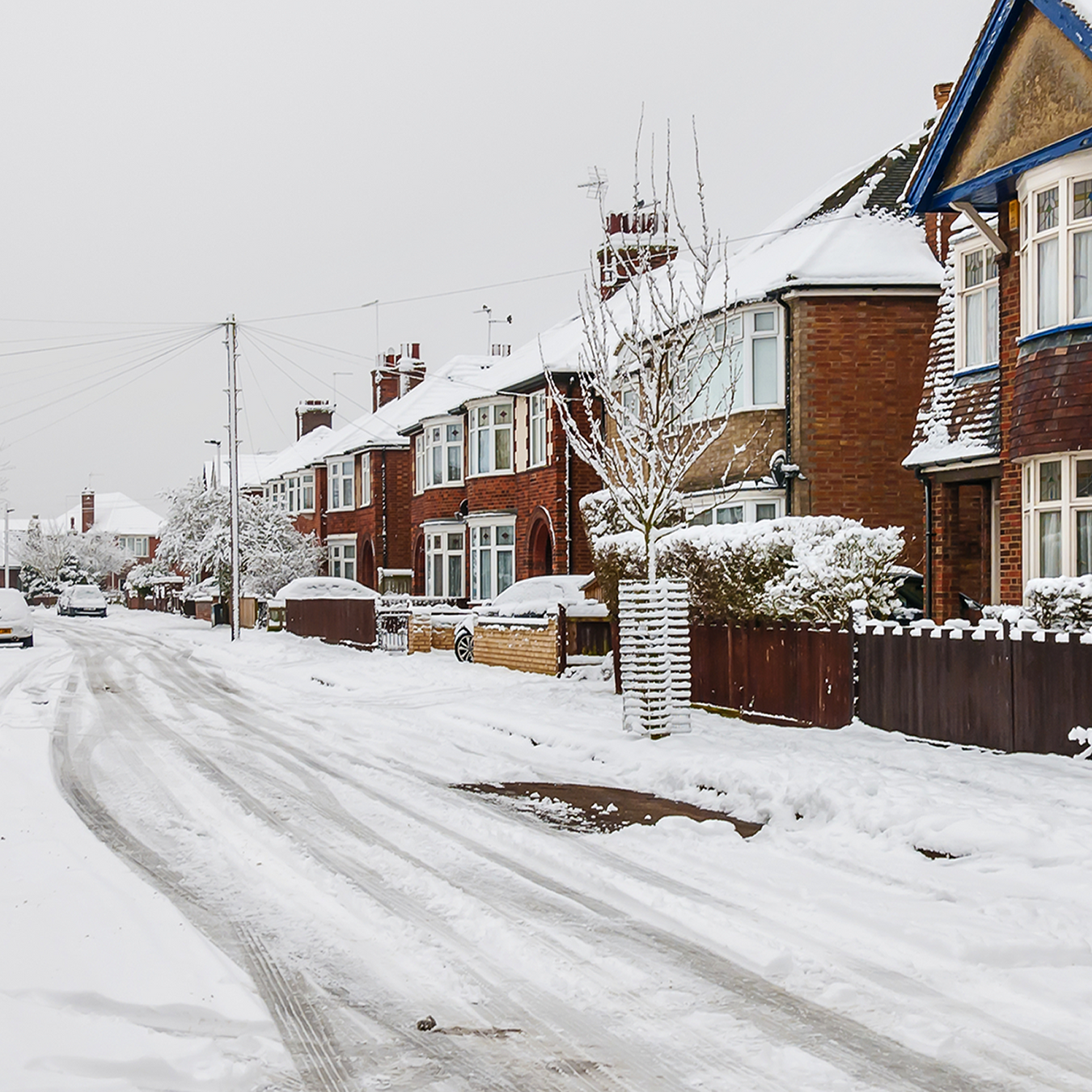 winter street scene showing houses with snow on the drive and pavement and a snowy uncleared road